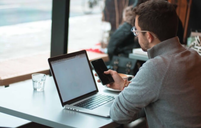 A man checking his phone with his laptop out.